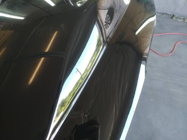 Glossy black car door reflecting a person and garage floor