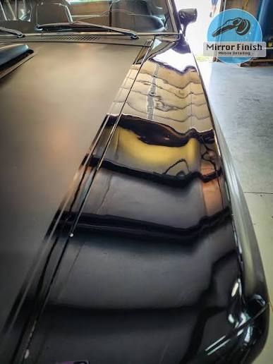Glossy black car hood reflecting a building and garage interior.