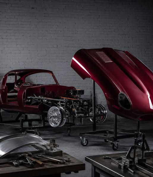 Classic car project in a workshop, with a red body shell and detached hood on stands.