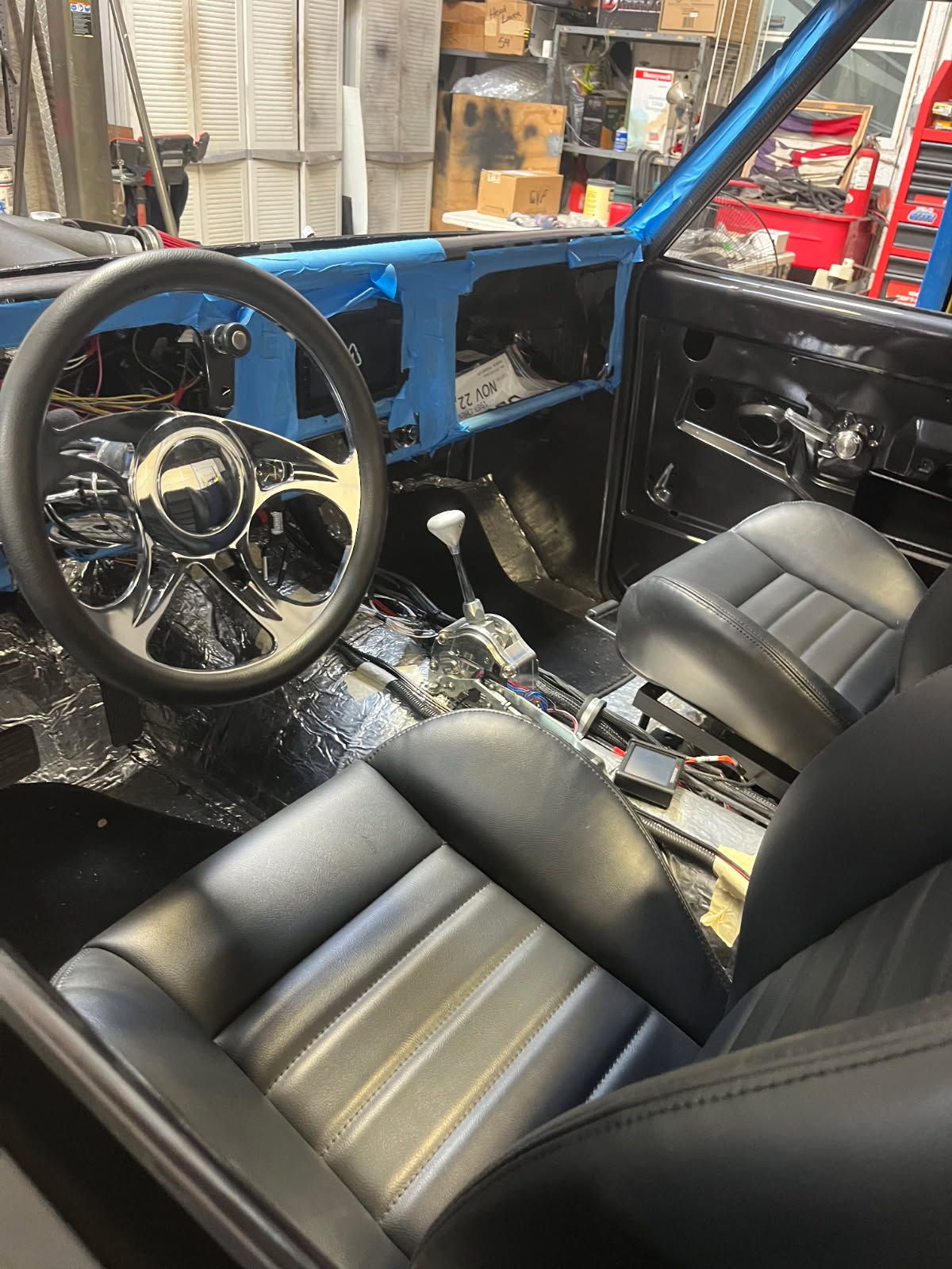 Custom car interior with black leather seats, steering wheel, and exposed blue frame in a garage