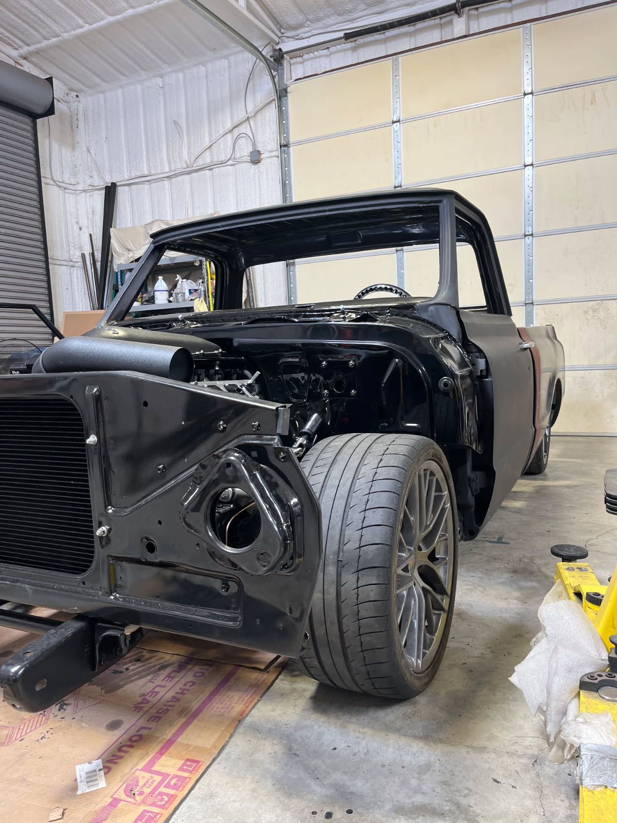 Partially restored black classic pickup truck in a workshop, front end exposed and missing body panels