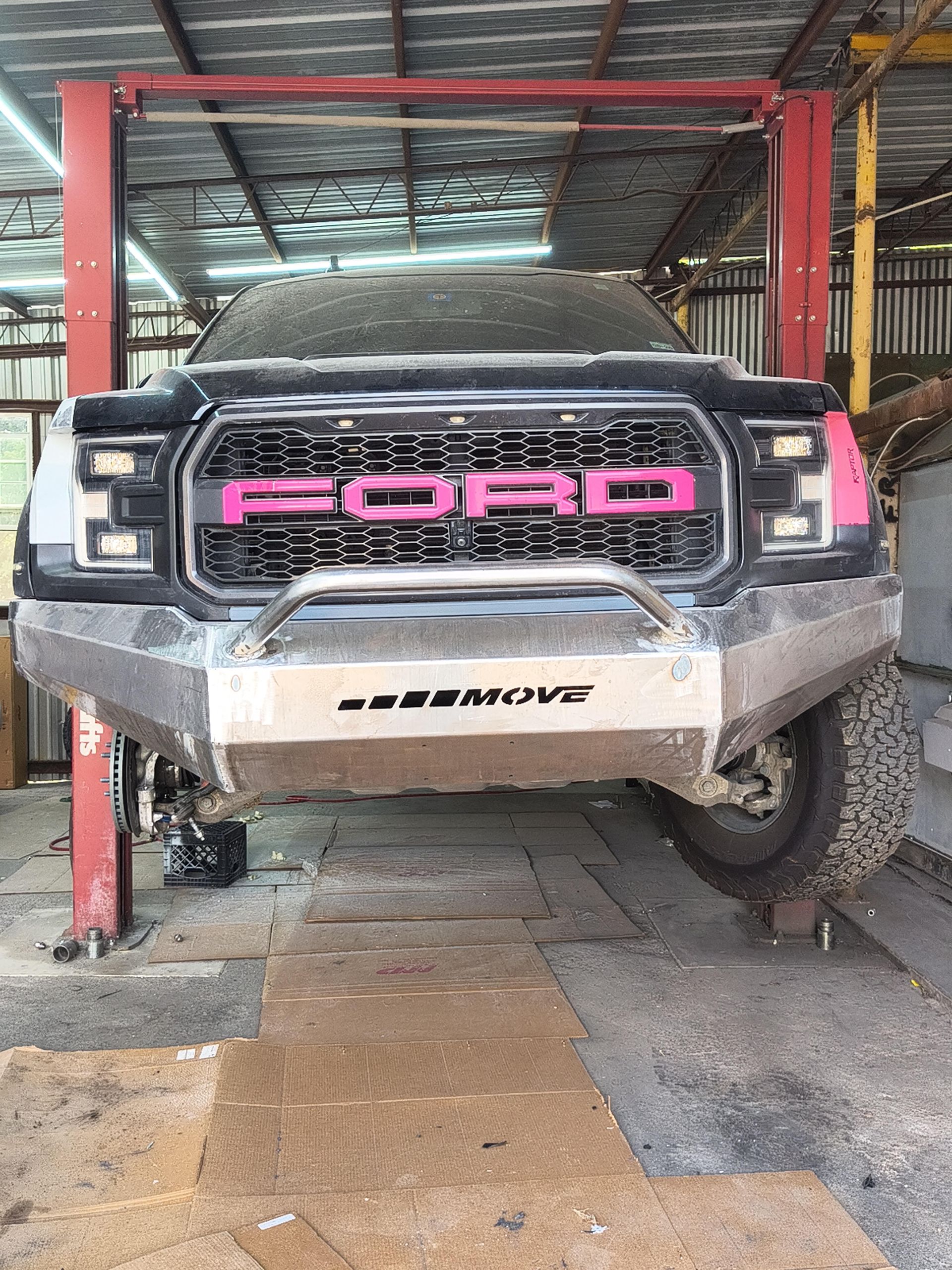 Pink FORD pickup truck parked under a covered area, front view with muddy bumper.