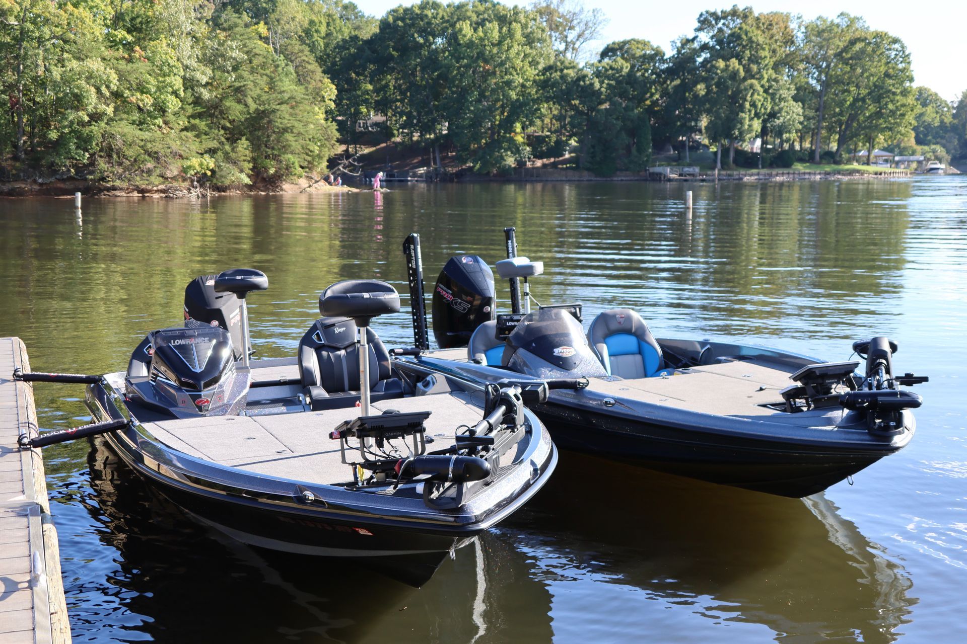 Two bass fishing boats docked on a calm river; green trees in the background.