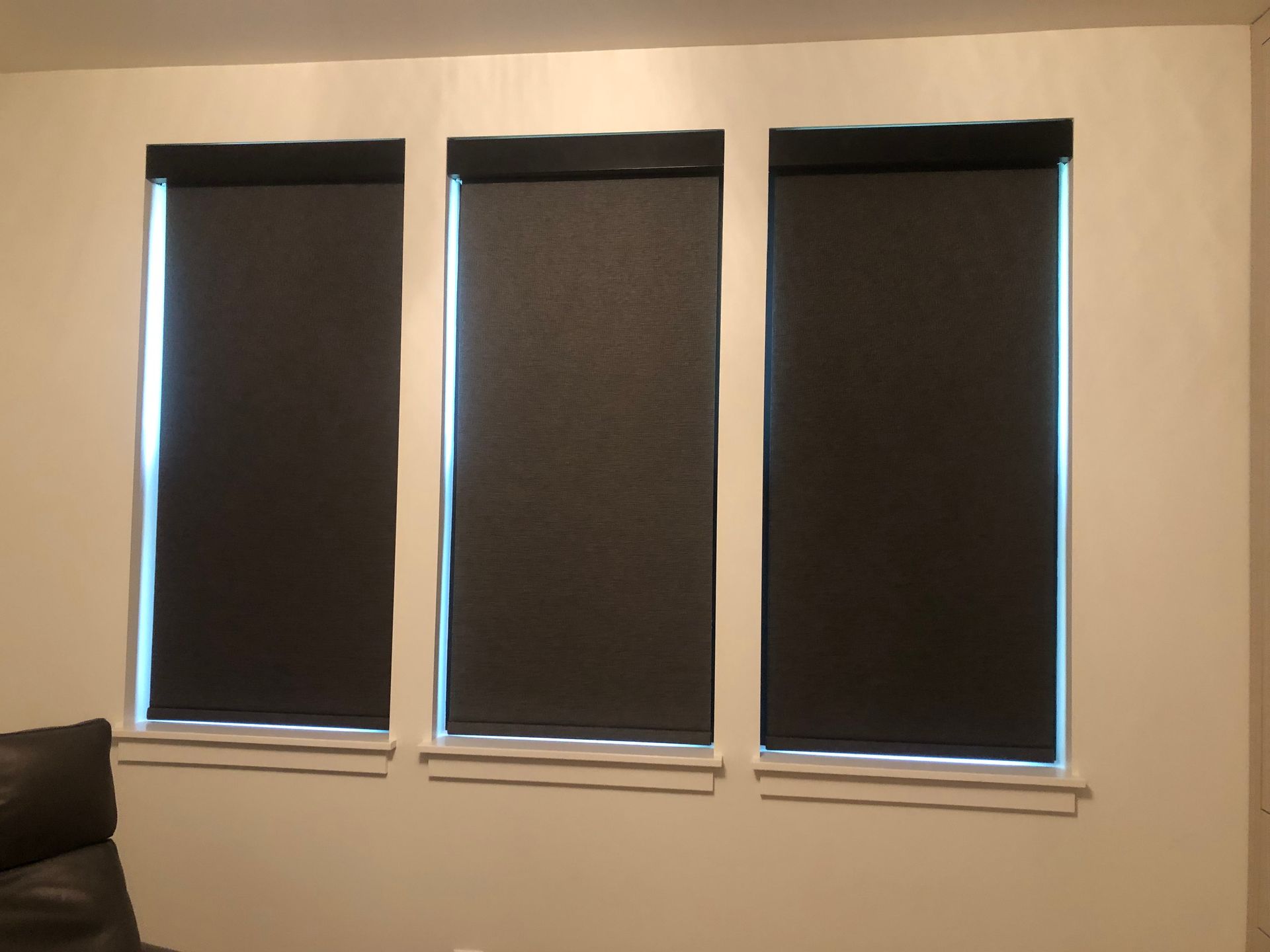 Three black blinds are hanging on a white wall in a living room.