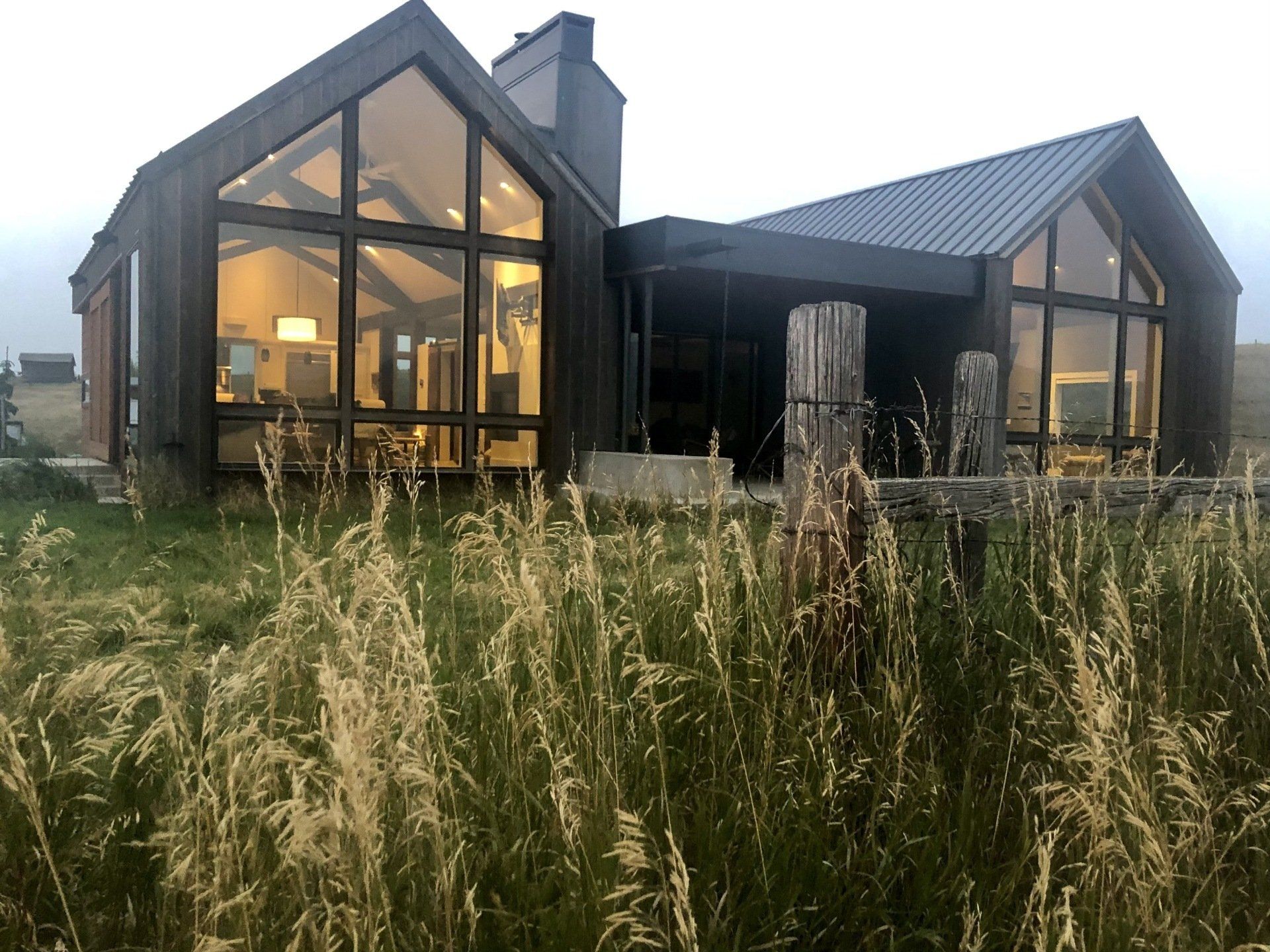 A house with a lot of windows is surrounded by tall grass