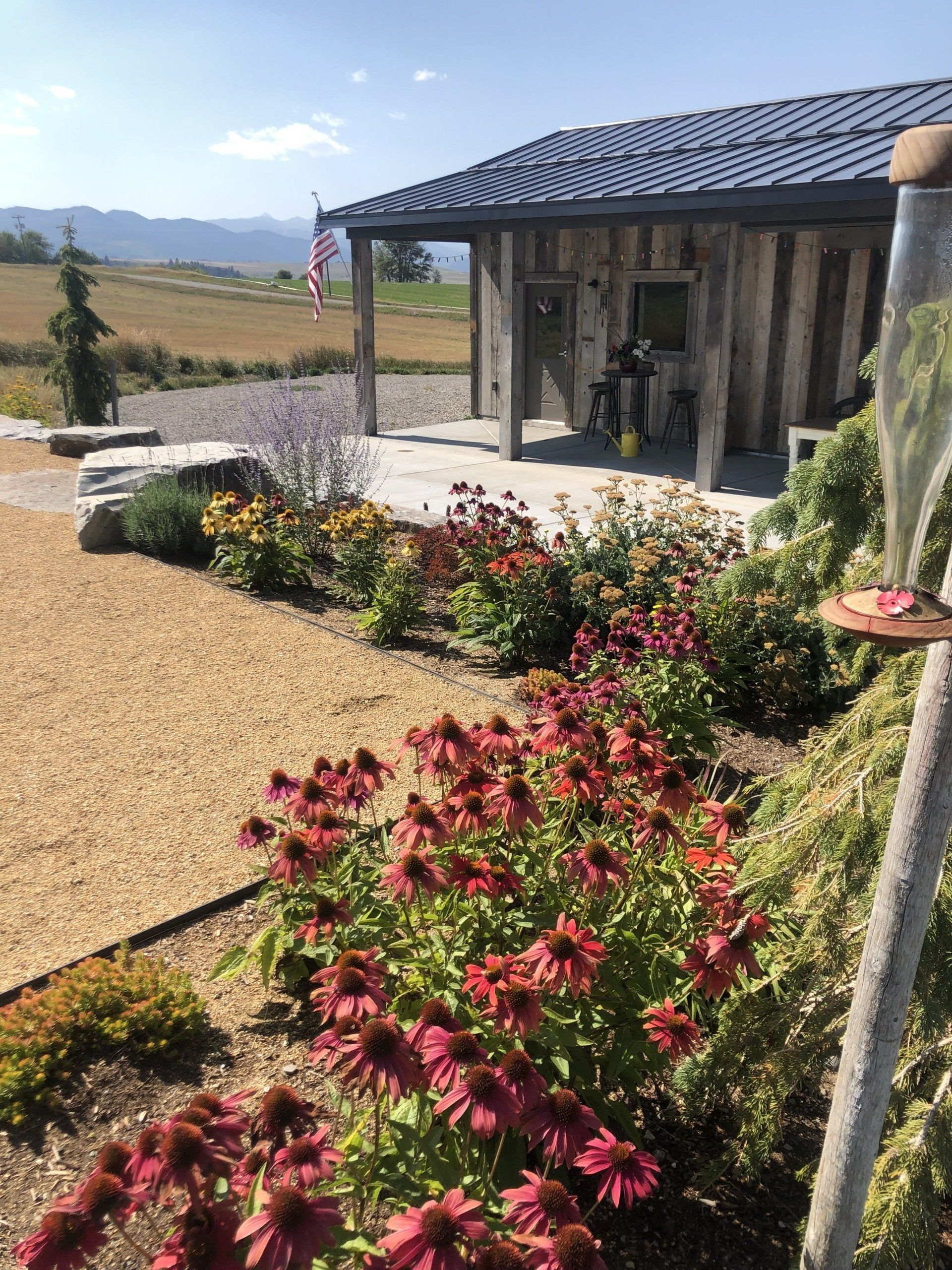 A bird feeder is sitting in front of a house surrounded by flowers.