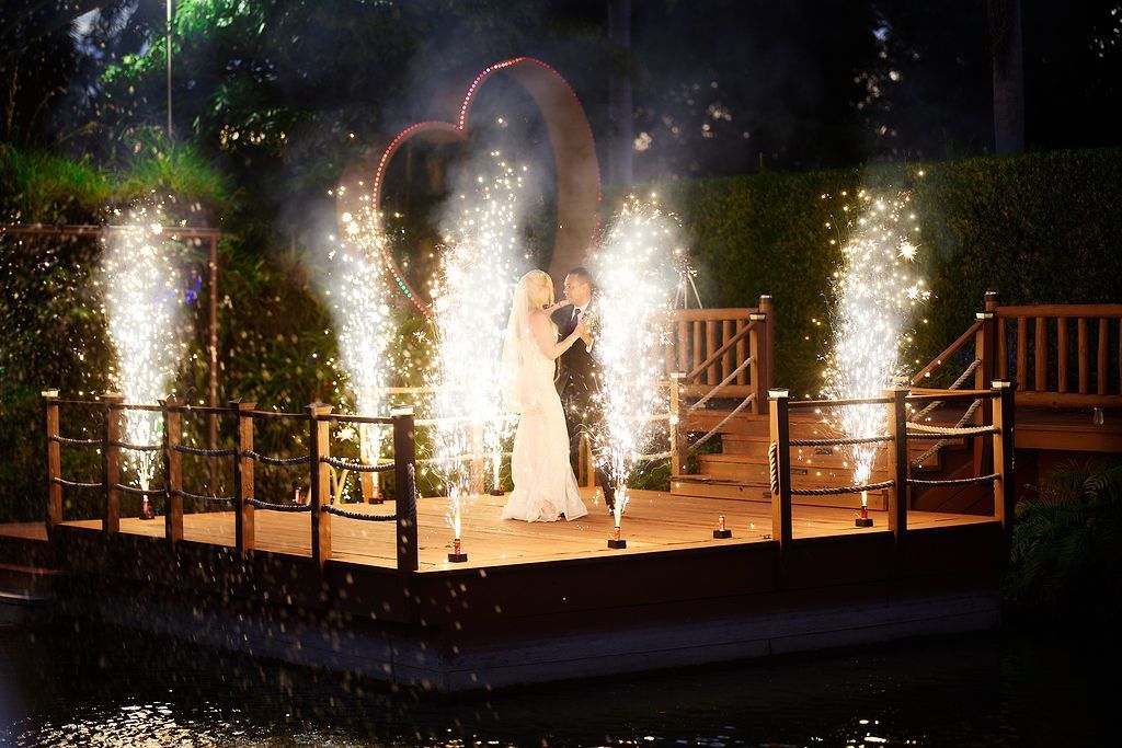 Couple kissing on a stage, fireworks erupting. A heart-shaped light and a water feature are visible.