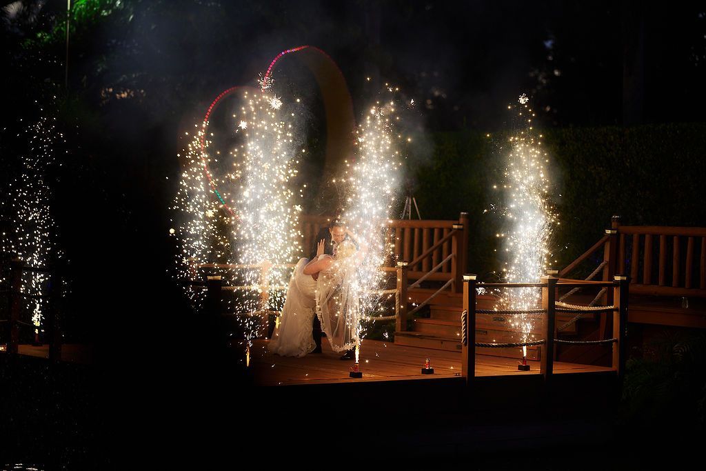 Couple under fireworks display forming a heart shape at a nighttime wedding.