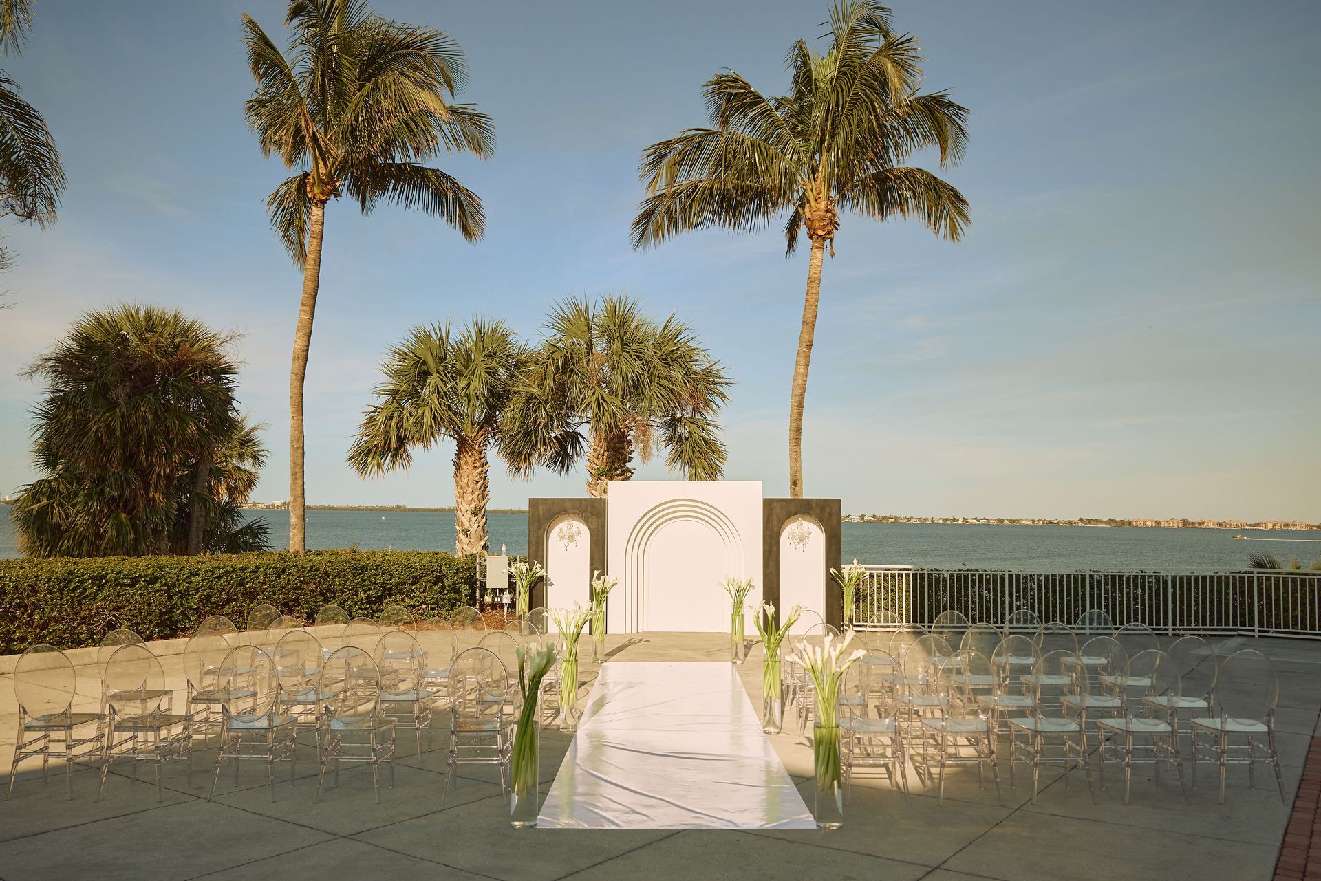 A wedding ceremony is taking place on the terrace at the Mansion at Tuckahoe with palm trees and Indian River Lagoon in the background