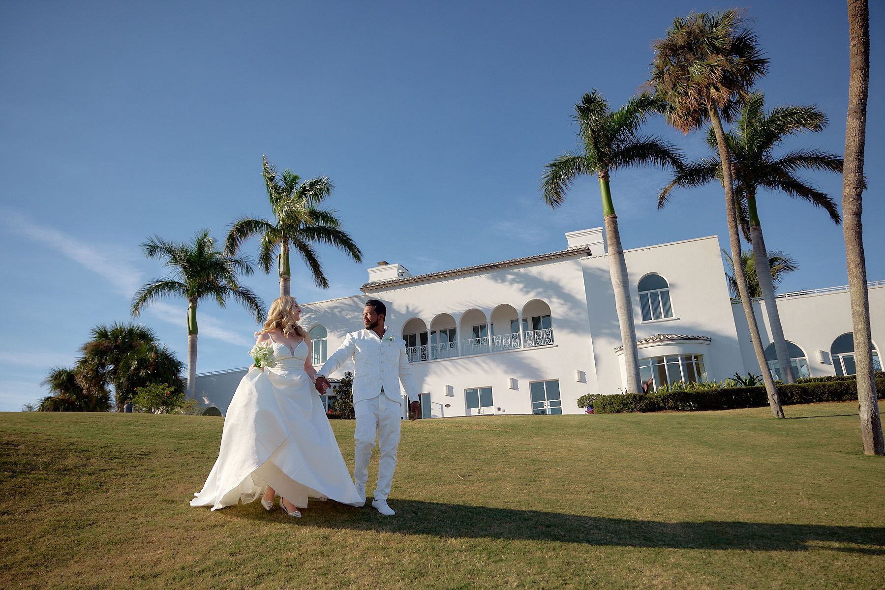 A bride and groom are walking in front of Mansion at Tuckahoe holding hands.
