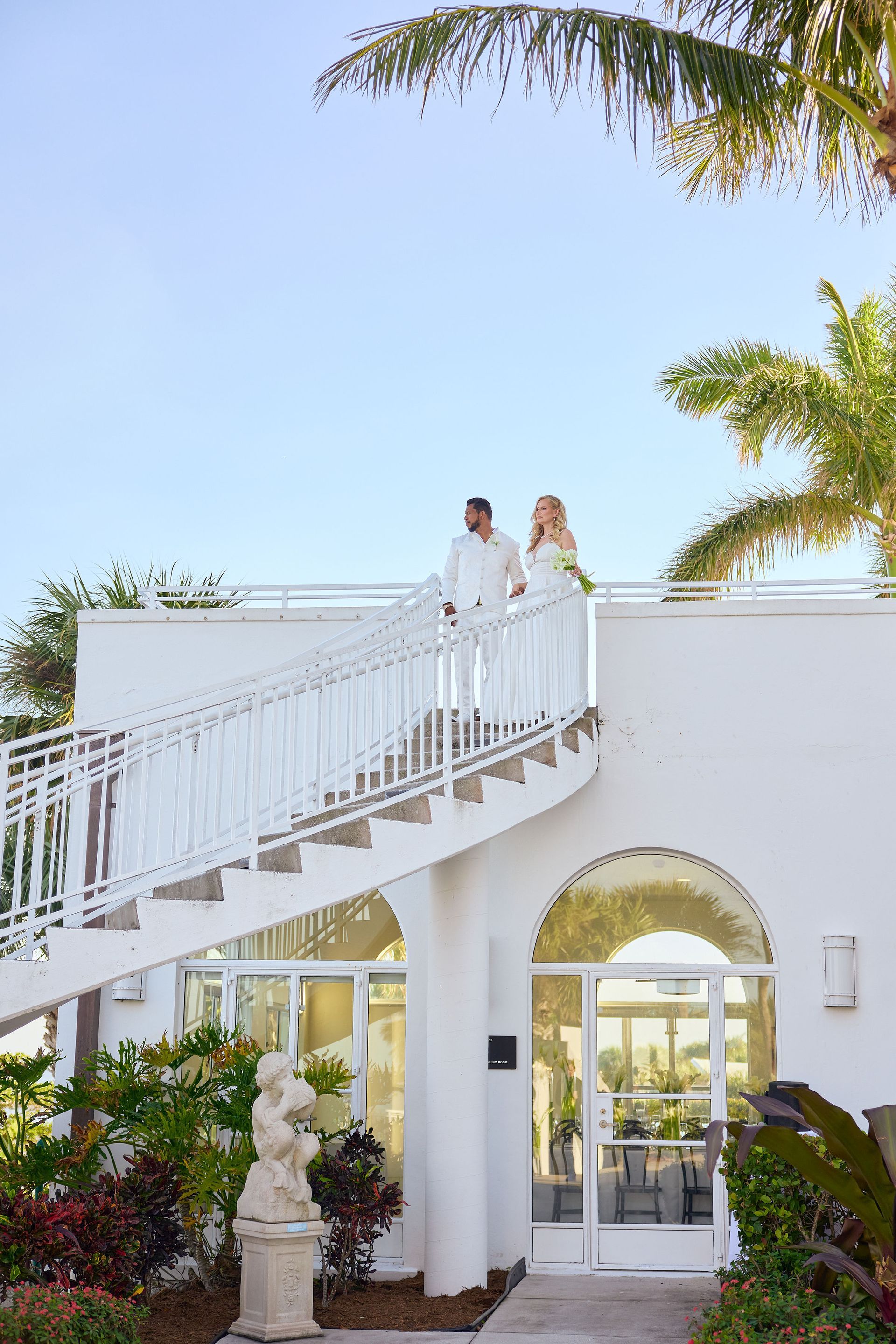 A bride and groom are standing on a balcony of a white building.