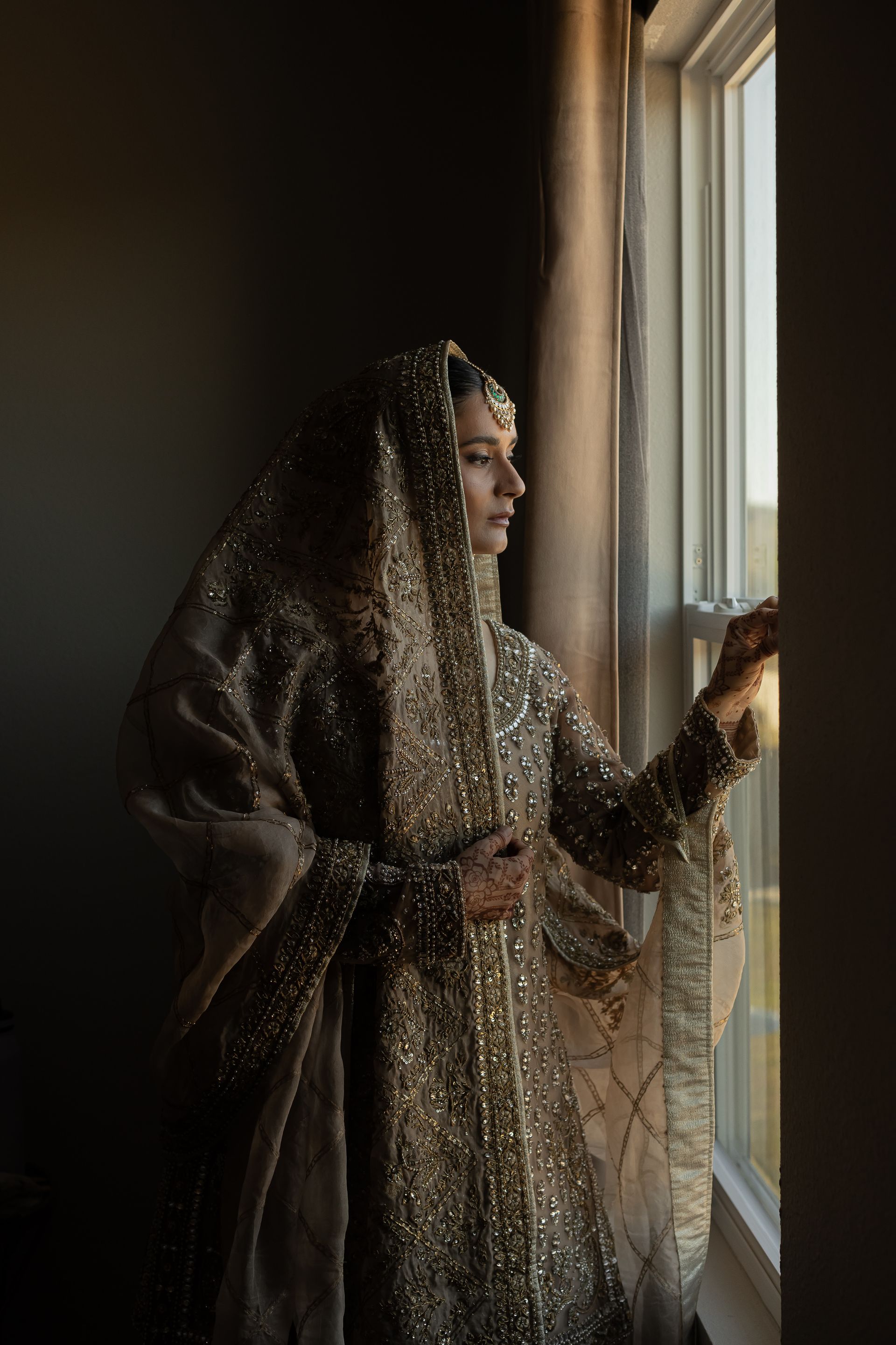 Woman in ornate gold gown looks out window.