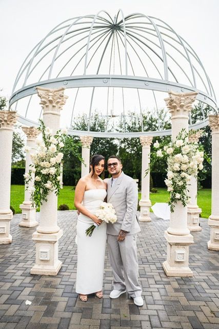 Couple posing in front of an outdoor gazebo with floral decorations.