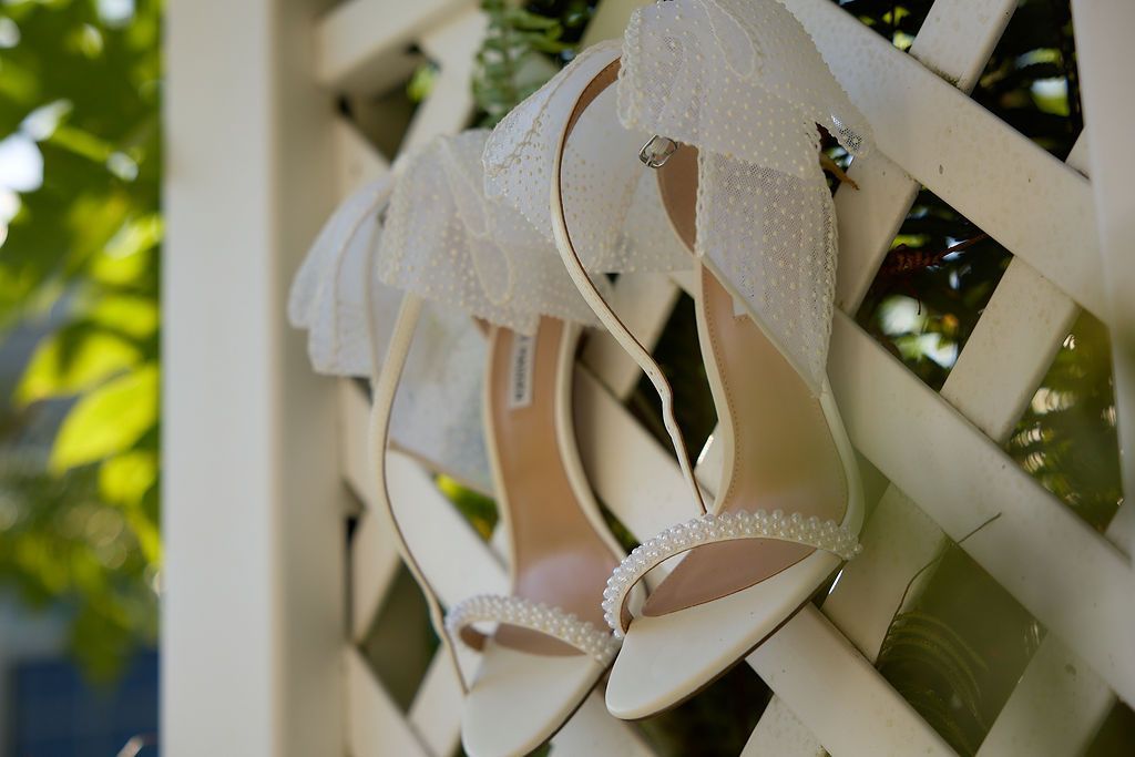 White wedding heels with lace detail hanging on a white lattice fence.