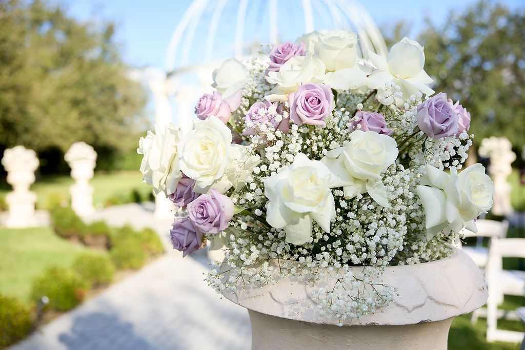White and lavender roses, greenery in a stone urn, set for an outdoor wedding.