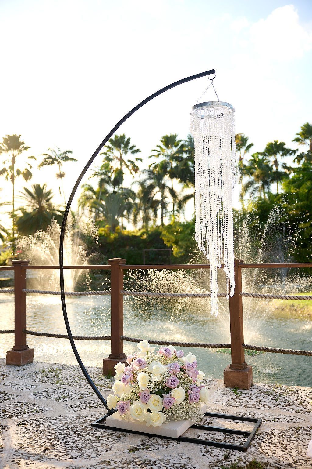 Black metal arch with crystal chandelier and floral arrangement in front of a fountain.