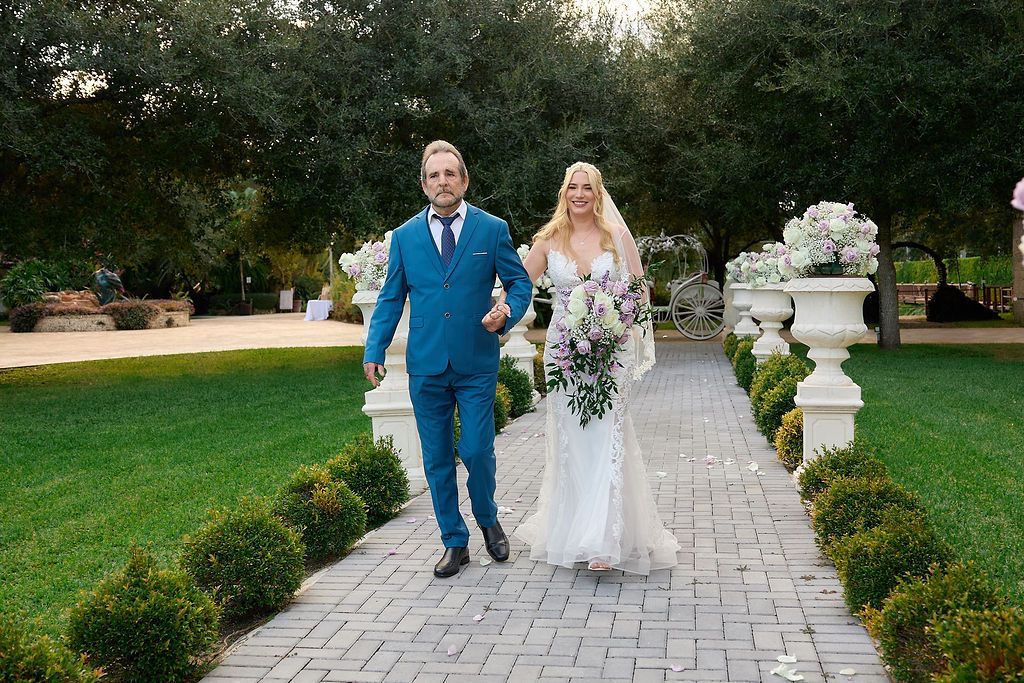 Man in teal suit and woman in white dress walk down a brick path after wedding.