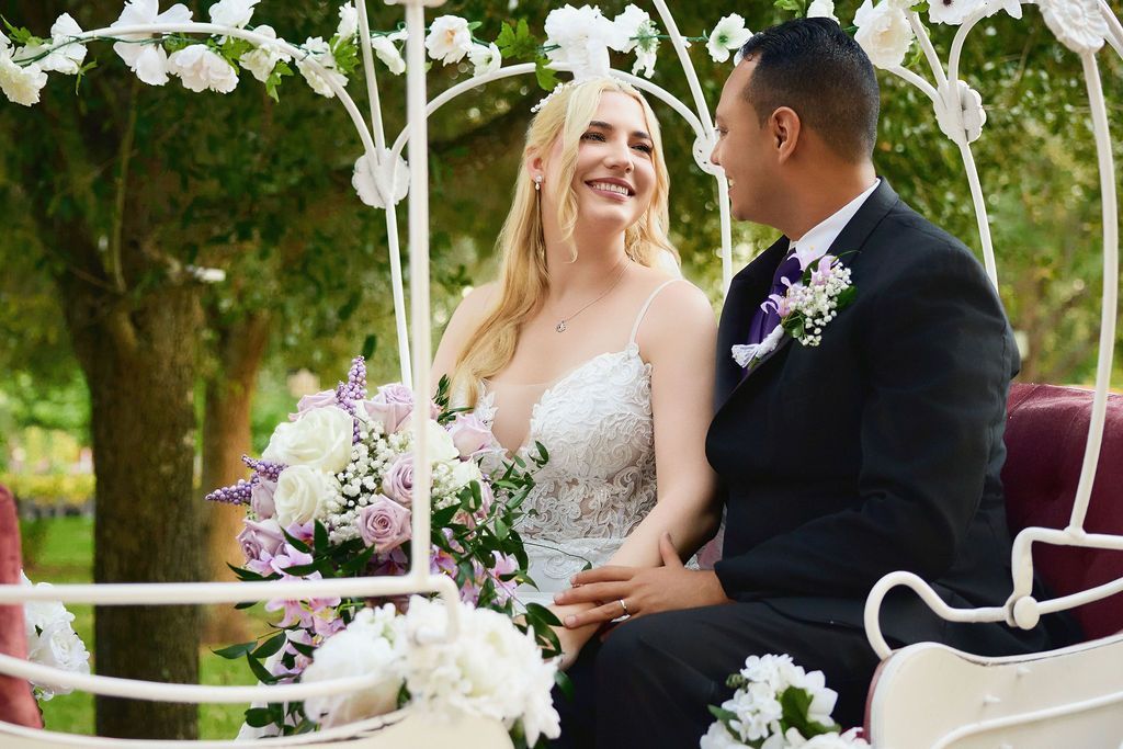 Bride and groom in a decorated horse-drawn carriage, smiling at each other.