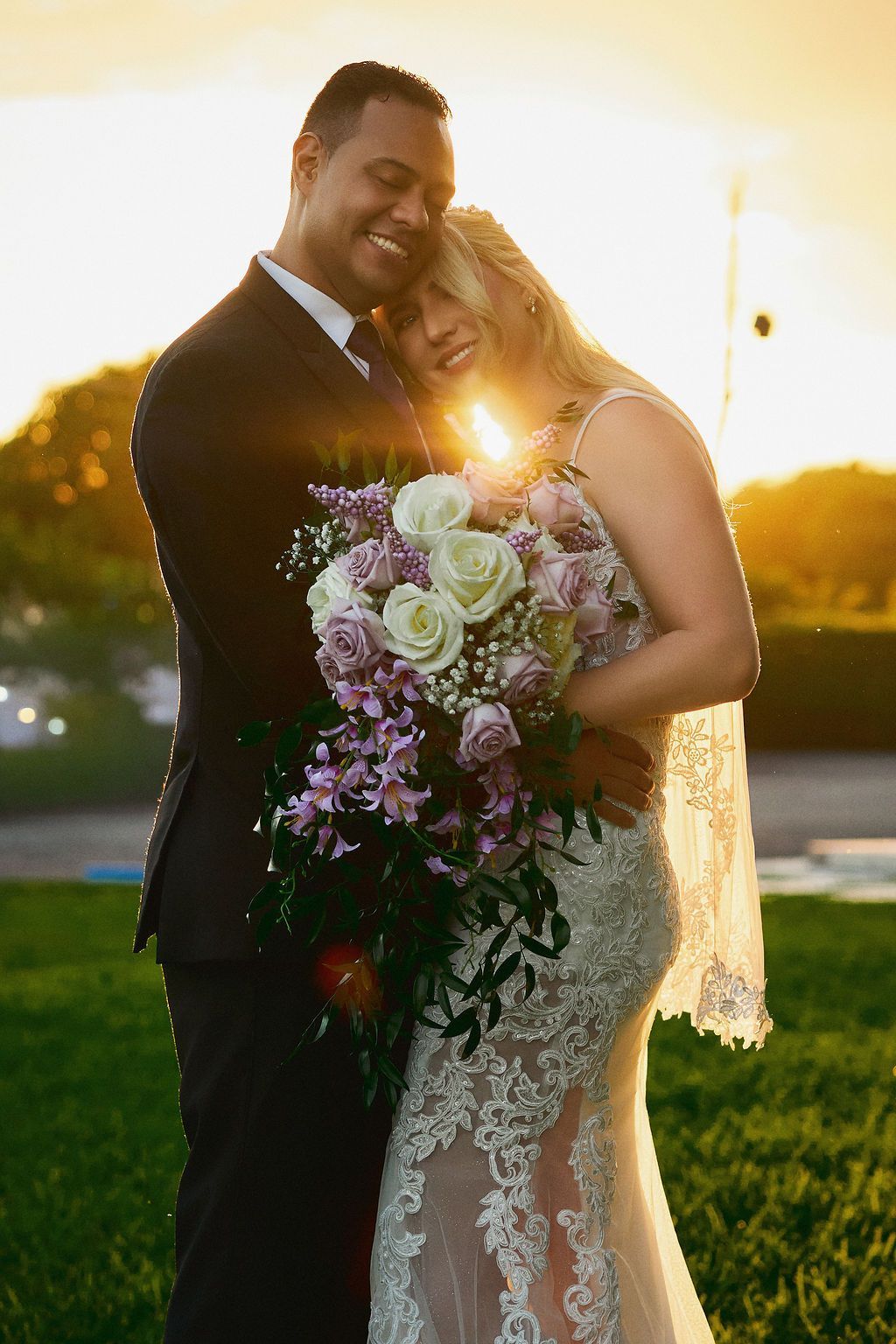 bride and groom hugging, bride holding a large cascading bouquet with white and lavender roses