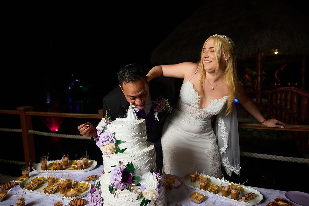Bride and groom playfully eating wedding cake. Nighttime outdoor setting.
