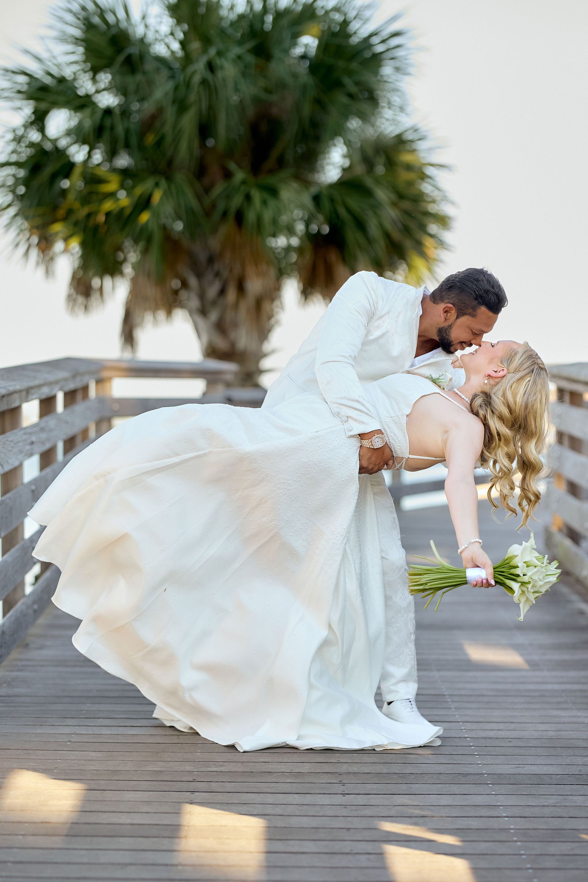 A bride and groom are kissing on a wooden bridge.