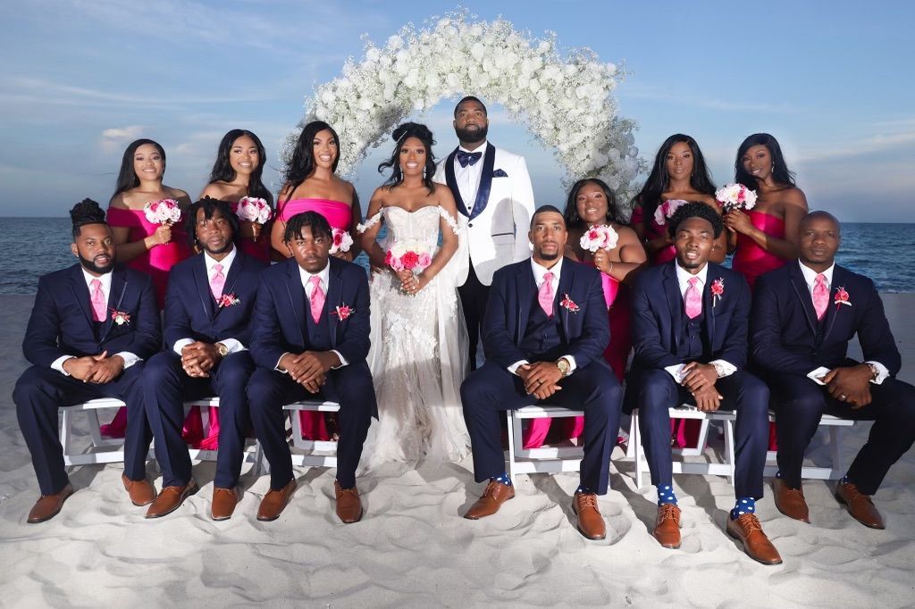 The bride and groom are posing for a picture with their wedding party on the beach.