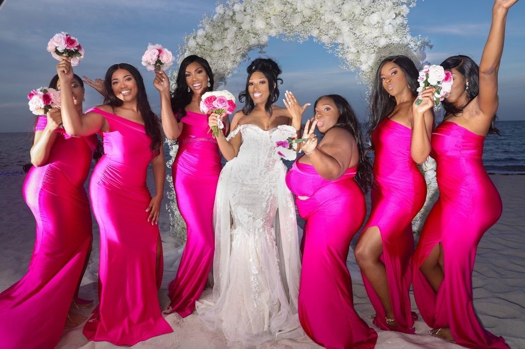 A bride and her bridesmaids are posing for a picture on the beach.