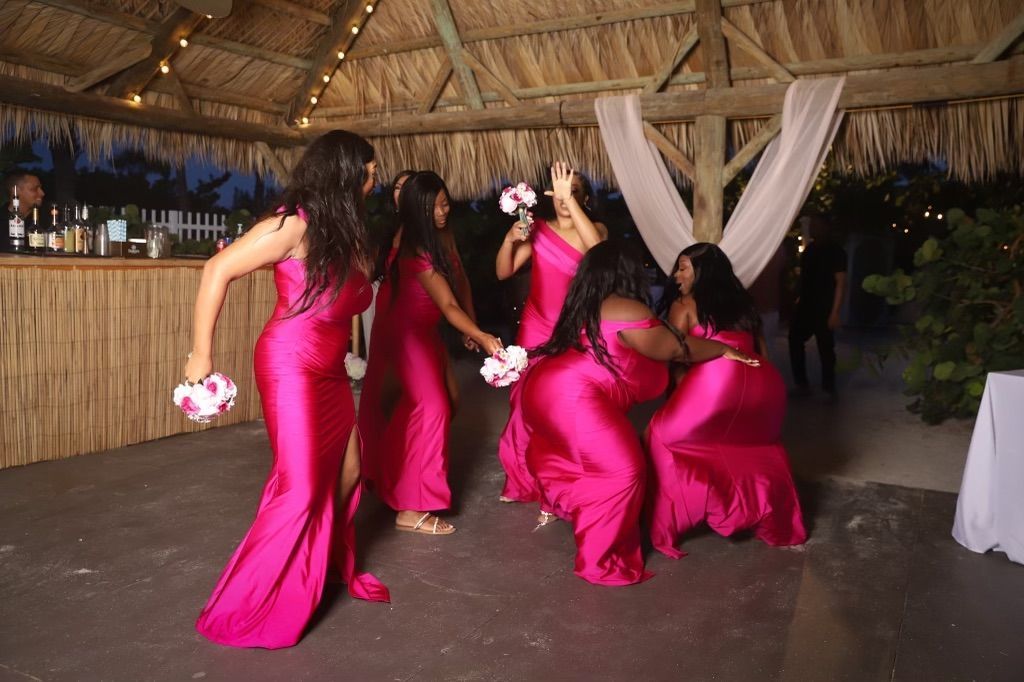 A group of women in pink dresses are dancing under a thatched roof.