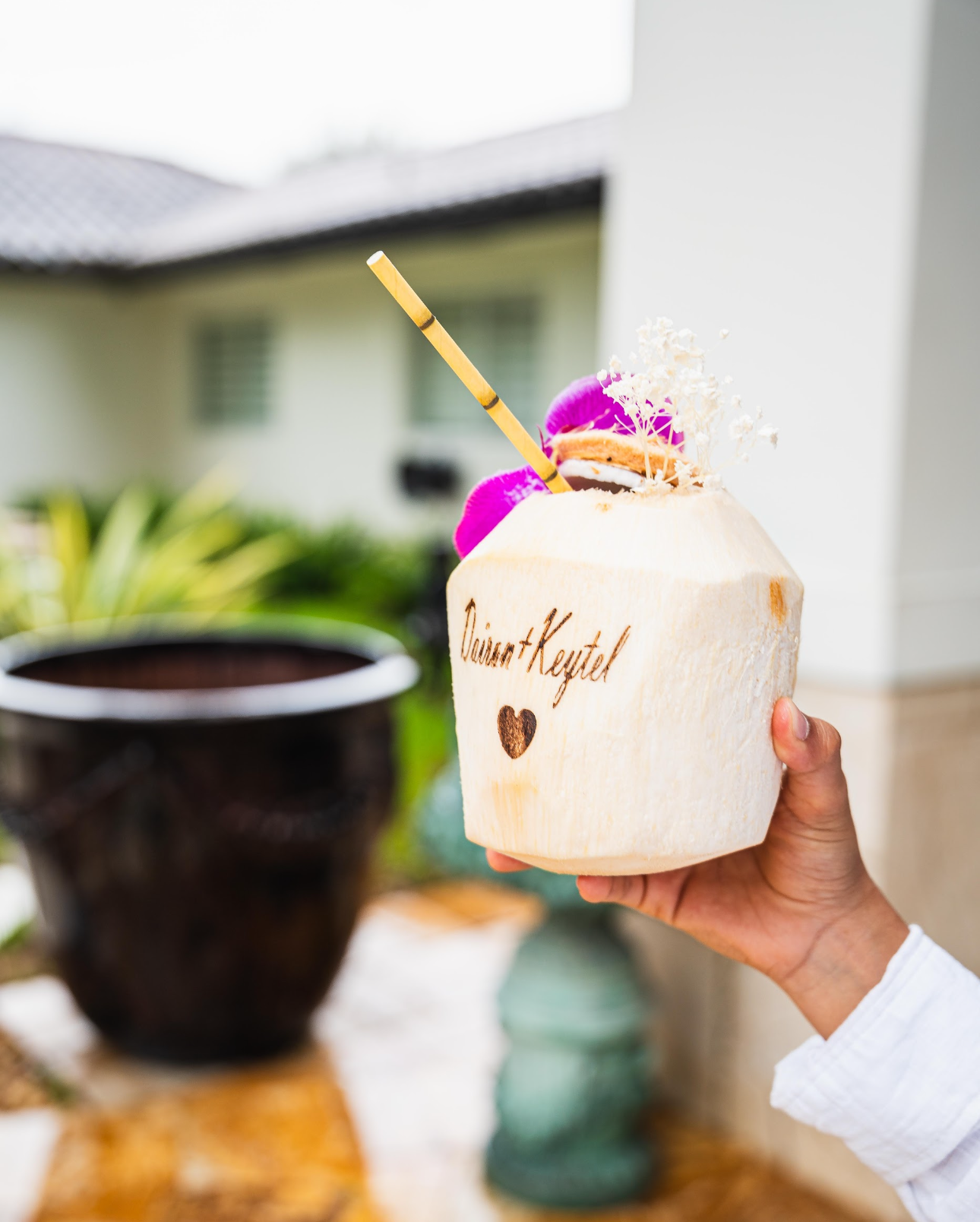 Hand holding a coconut cocktail with a straw, flowers, and 