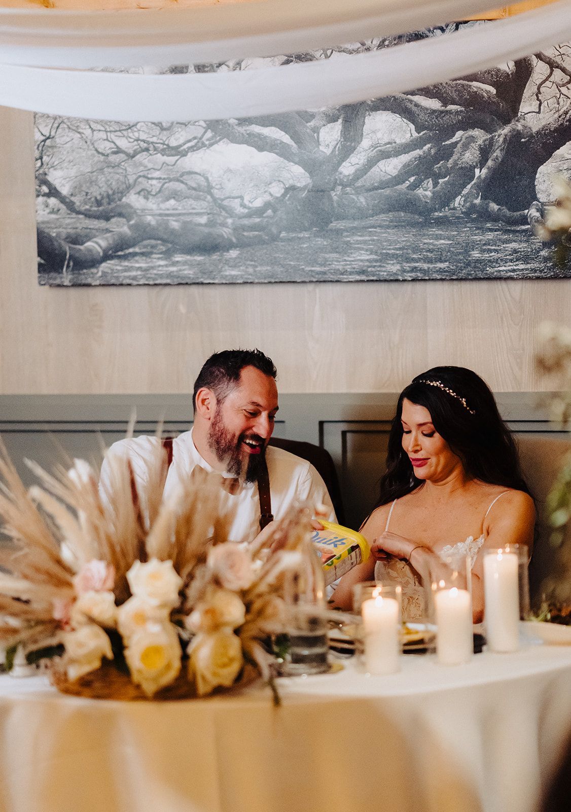 A bride and groom are sitting at a table with candles and flowers.