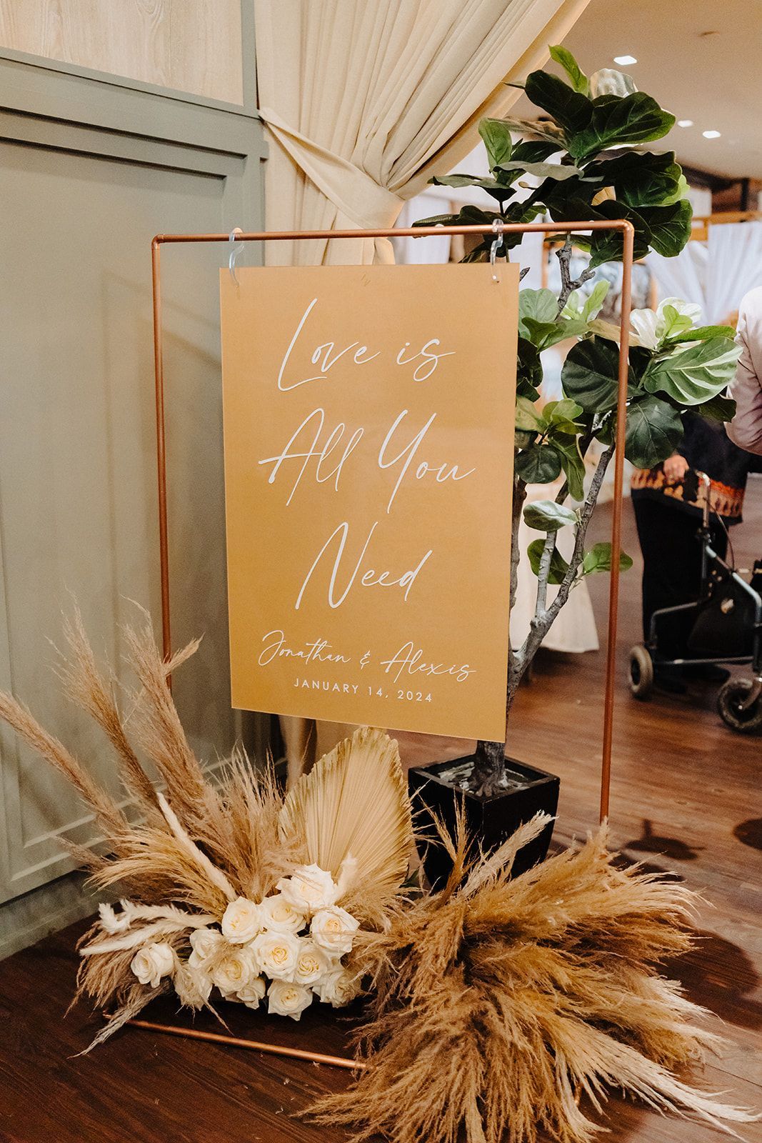 A sign that says `` love is all you need '' is surrounded by flowers and plants.