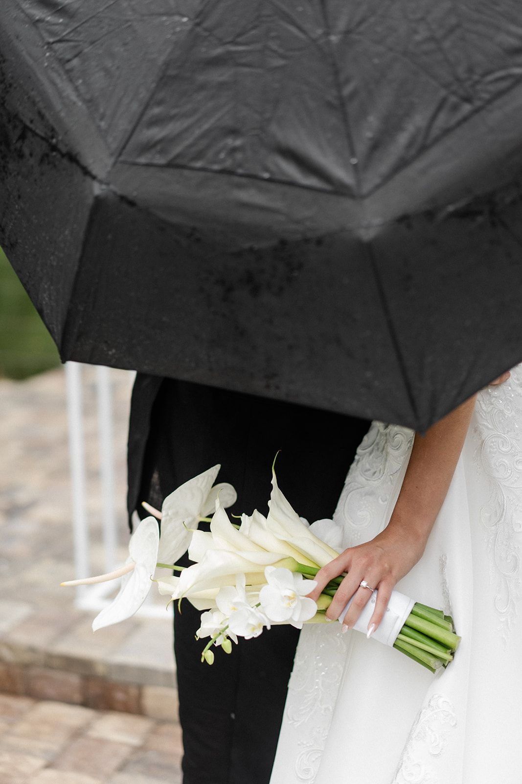 Bride and groom under a black umbrella; bride holds a white bouquet.