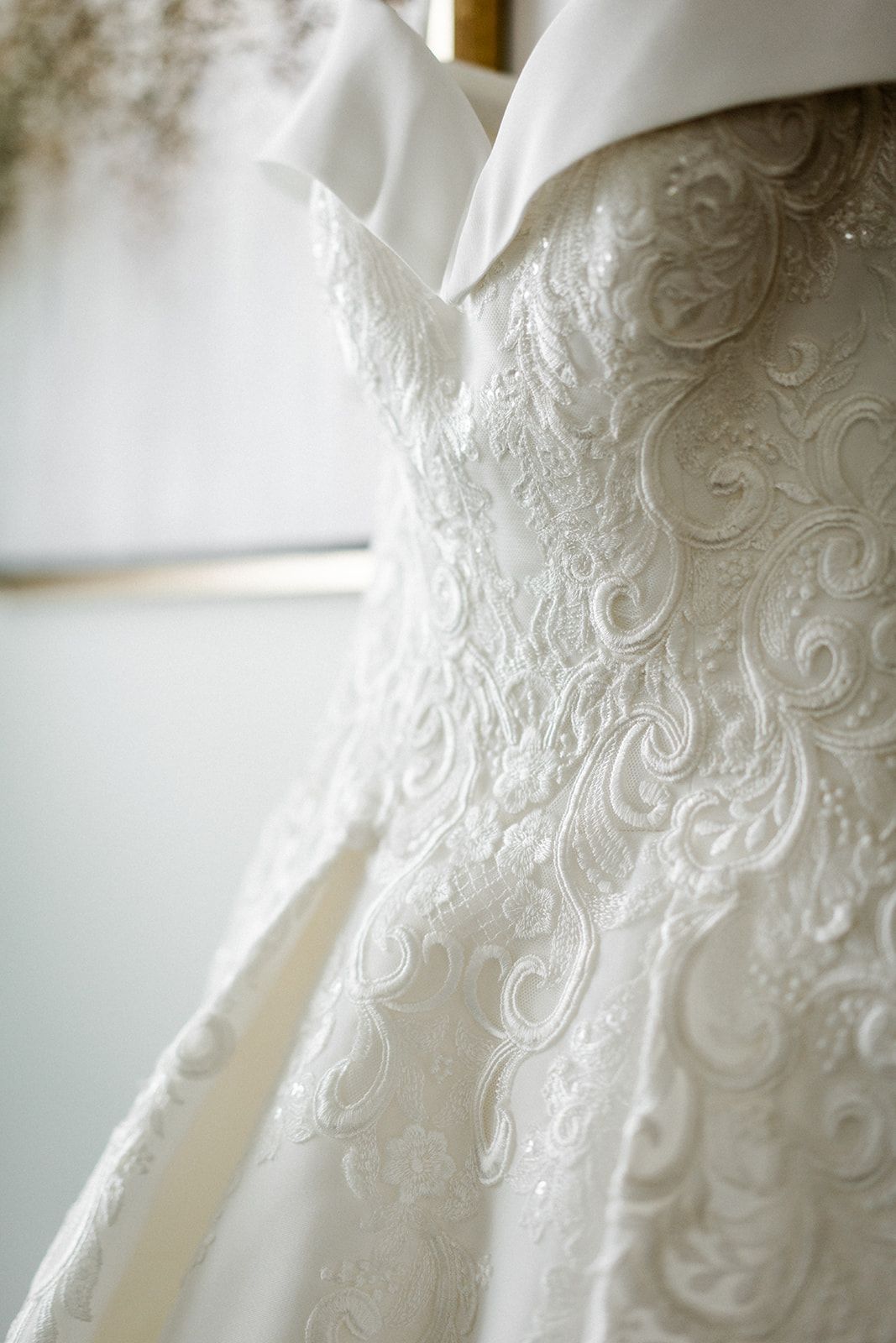 Close-up of a white wedding dress with detailed lace embroidery hanging on a rack.