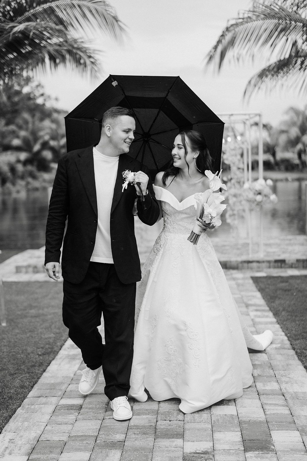 Newly married couple walking under an umbrella, smiling. Outdoor wedding ceremony.