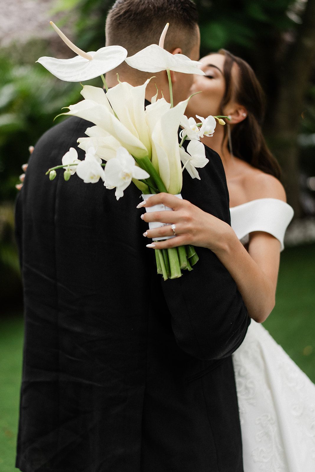 Bride kissing groom, holding white flower bouquet; outdoor wedding, close-up.