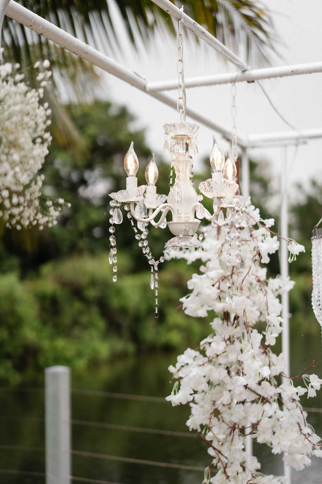 Chandelier decorated with white flowers hanging from a white frame, with a natural, green background.