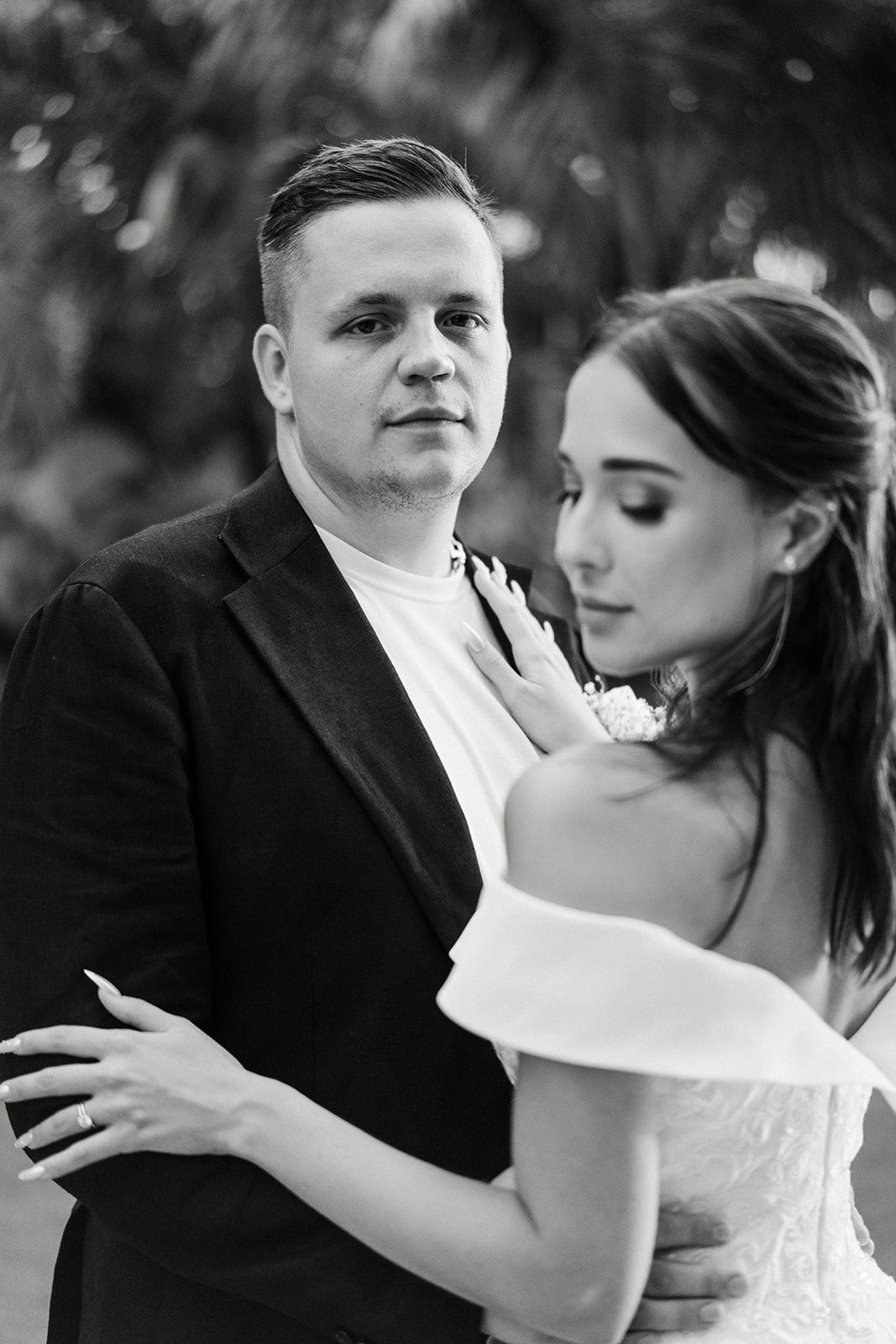 A couple, possibly at a wedding, in black and white. The man wears a blazer, the woman a white gown.