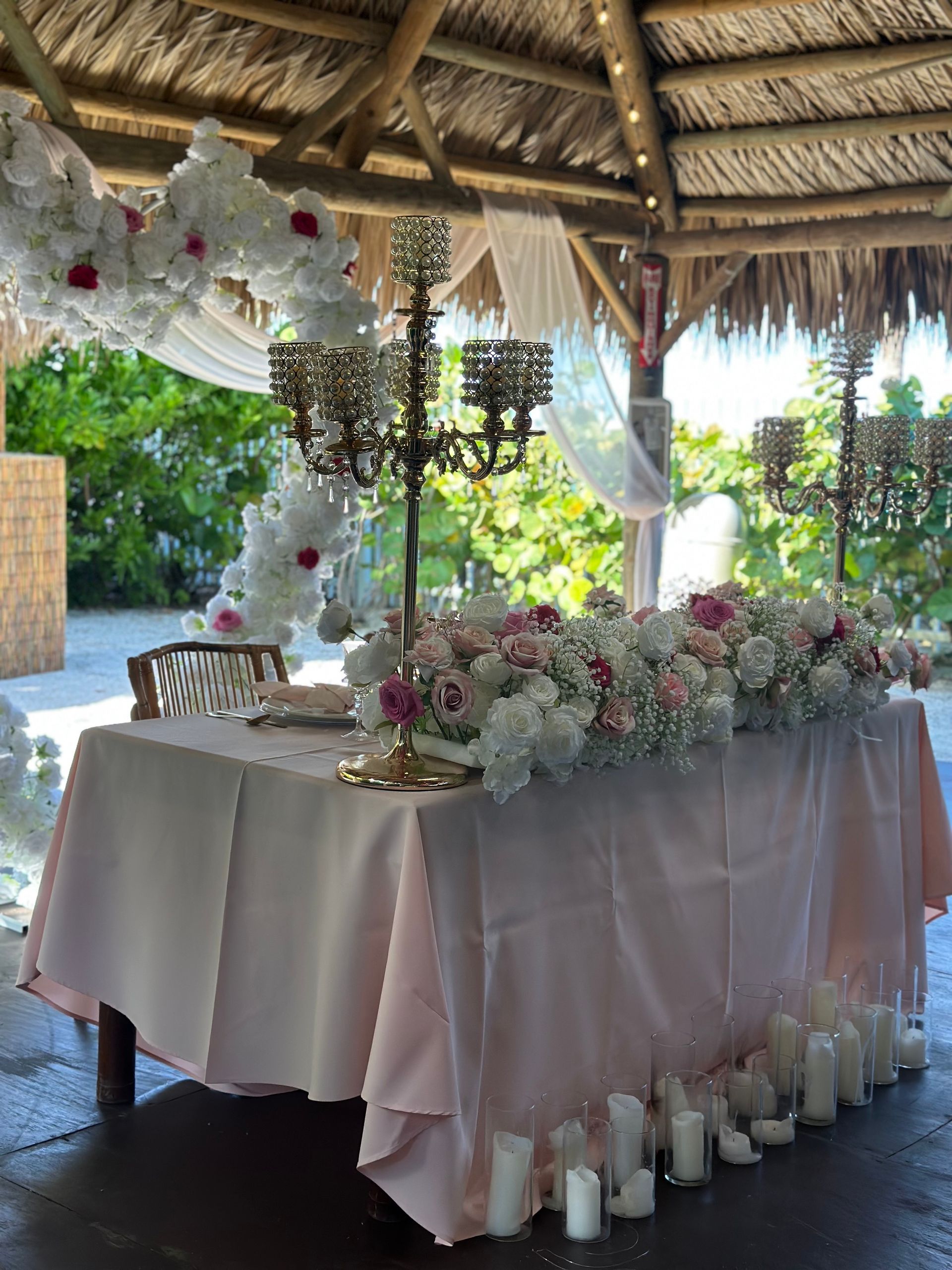 A long table with candles and flowers on it under a gazebo.