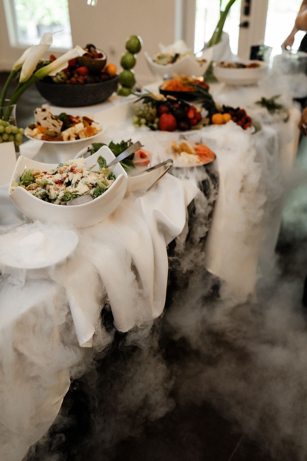 Buffet table with various food dishes, covered in dry ice creating a misty, cloud-like effect.
