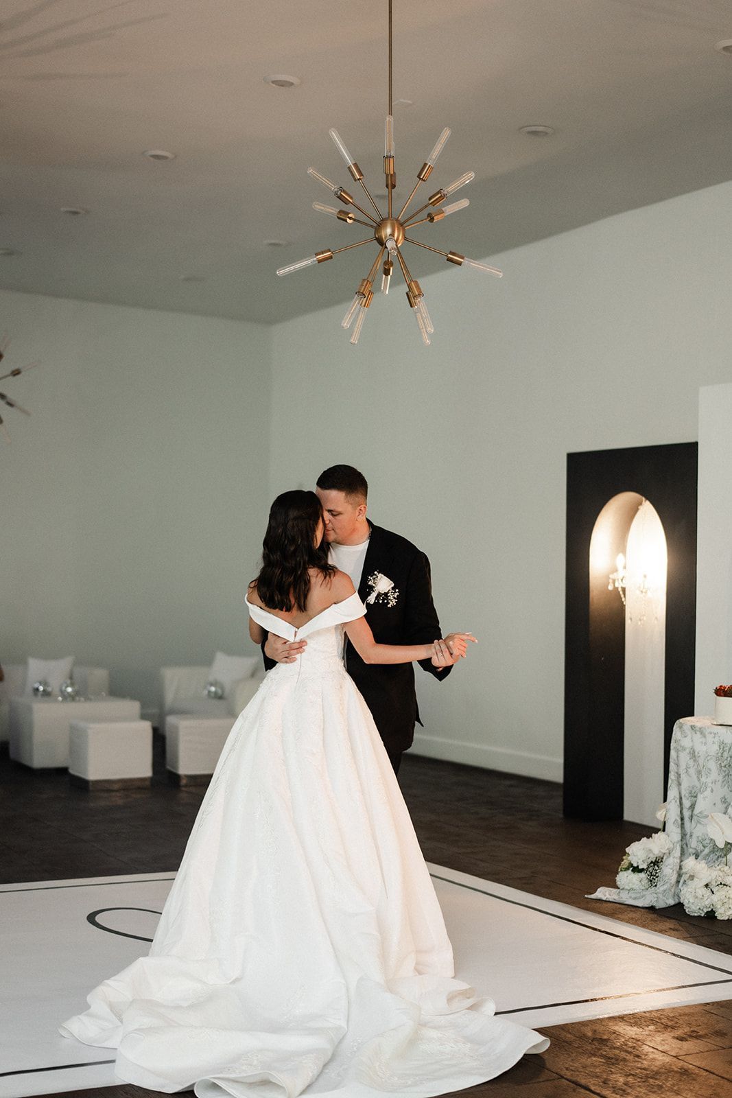 Couple dancing at a wedding reception under a starburst chandelier, a large white dress, black suit.