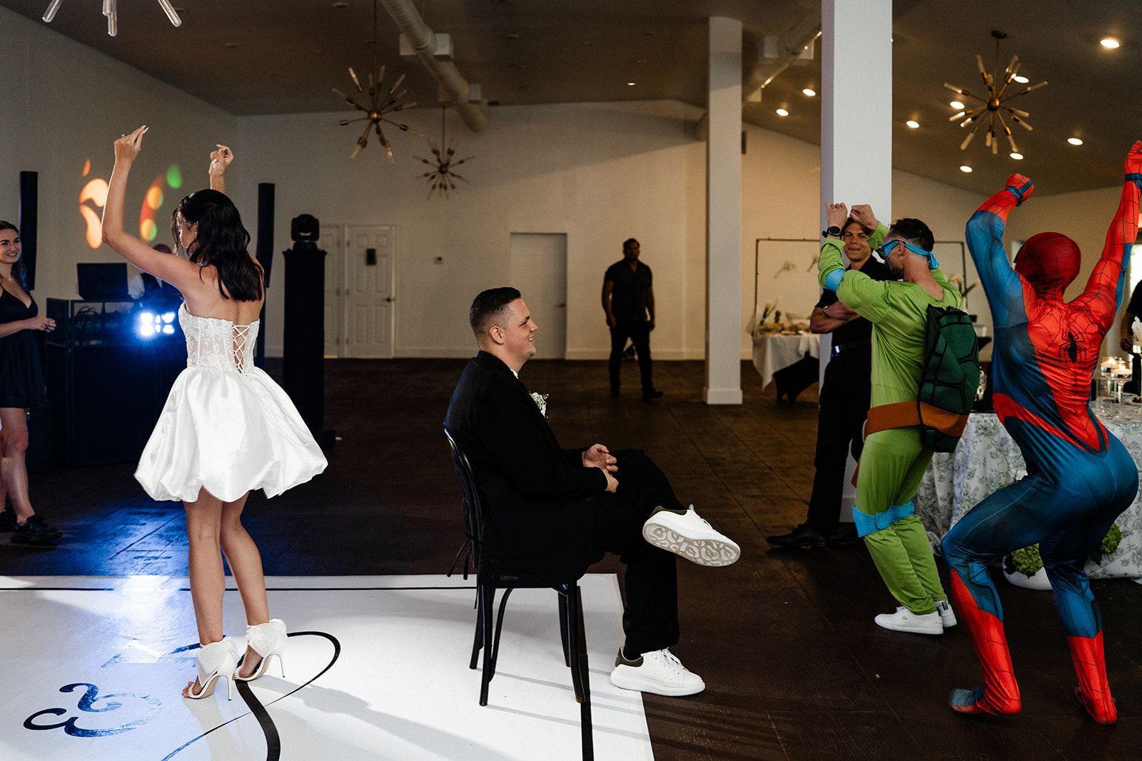 Bride dancing at a party as guests in costumes like Spider-Man and a Ninja Turtle celebrate.
