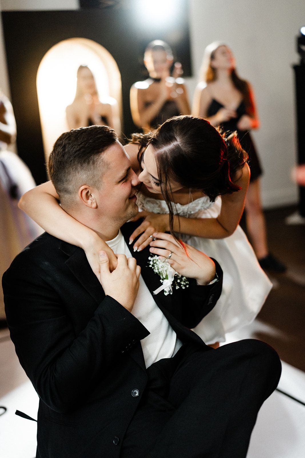 Couple embracing; woman leaning in to kiss man. Black suit, white dress, indoor setting.