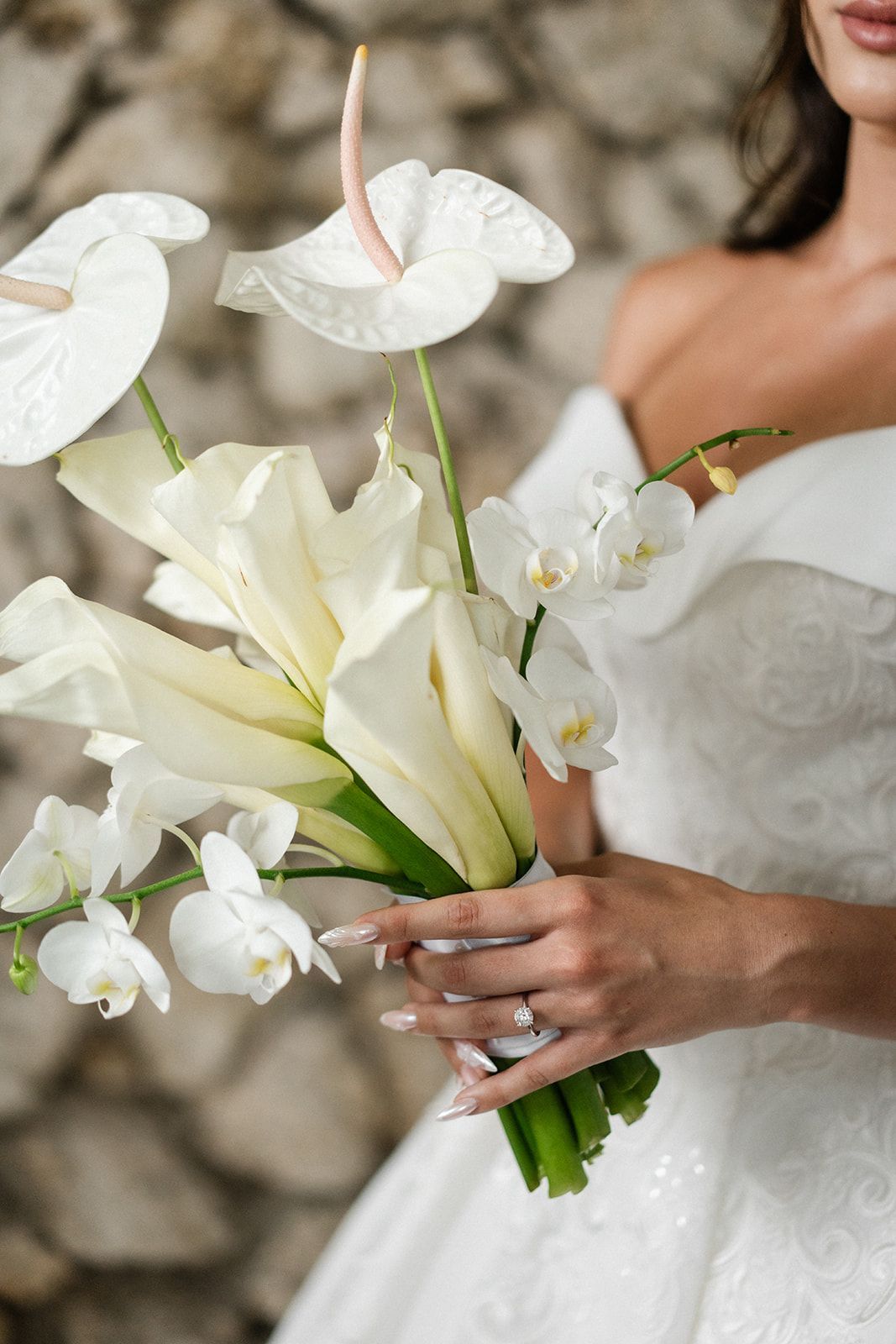 Woman in white dress holds a bouquet of white calla lilies, orchids, and anthuriums.