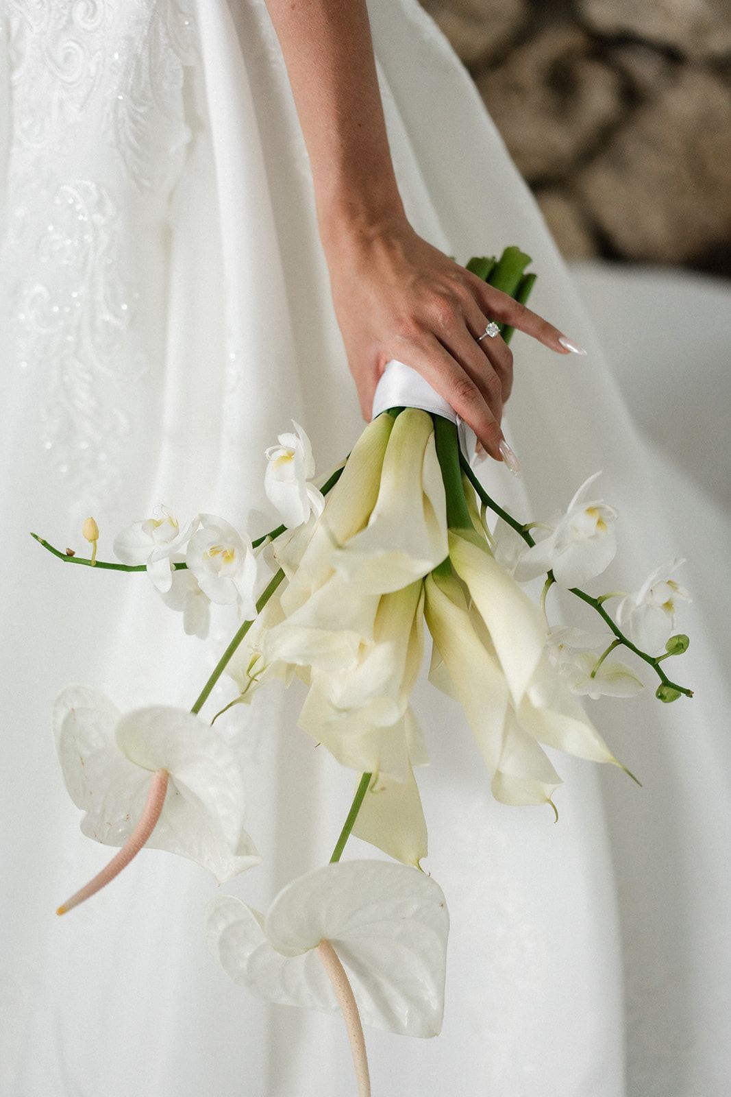 Bride holding a bouquet of white calla lilies, orchids, and anthurium, wearing a white wedding dress.
