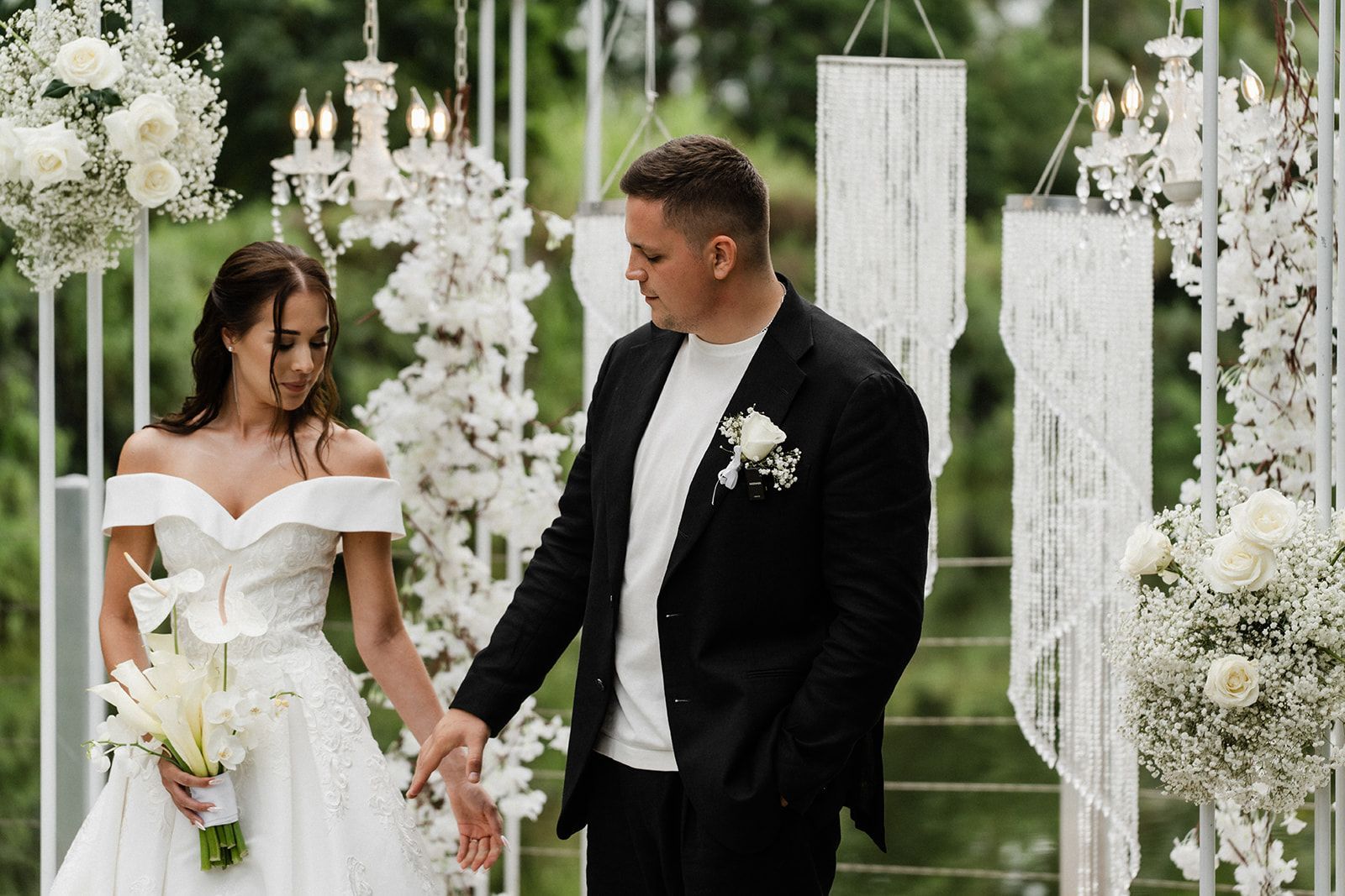 Couple holding hands at outdoor wedding ceremony; bride in white gown, groom in black suit.