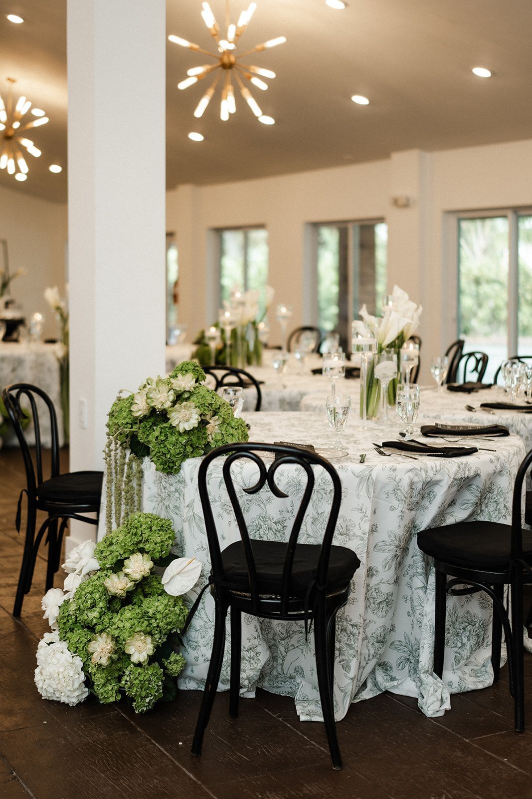 Elegant wedding reception with round tables, black chairs, and floral centerpieces.