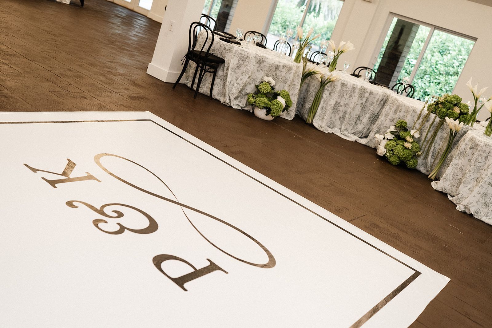 White dance floor with gold initials and infinity symbol, tables set for a wedding.