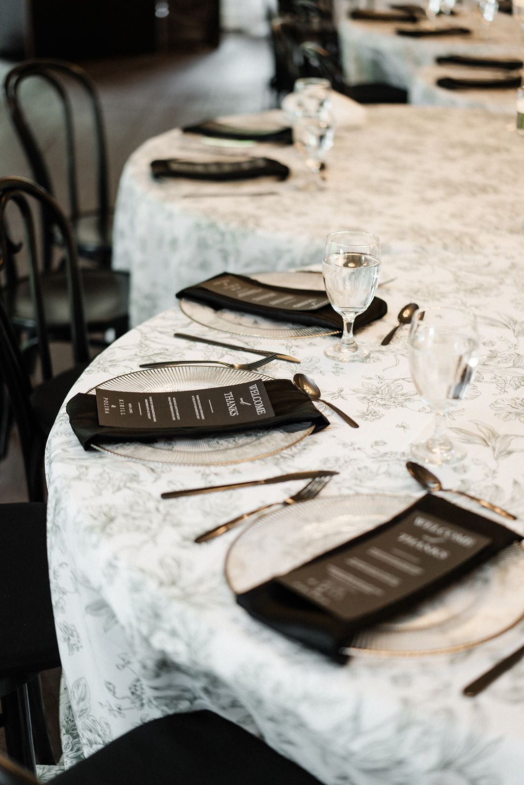 Round tables set with silverware, black napkins, menus, and water glasses; black chairs.