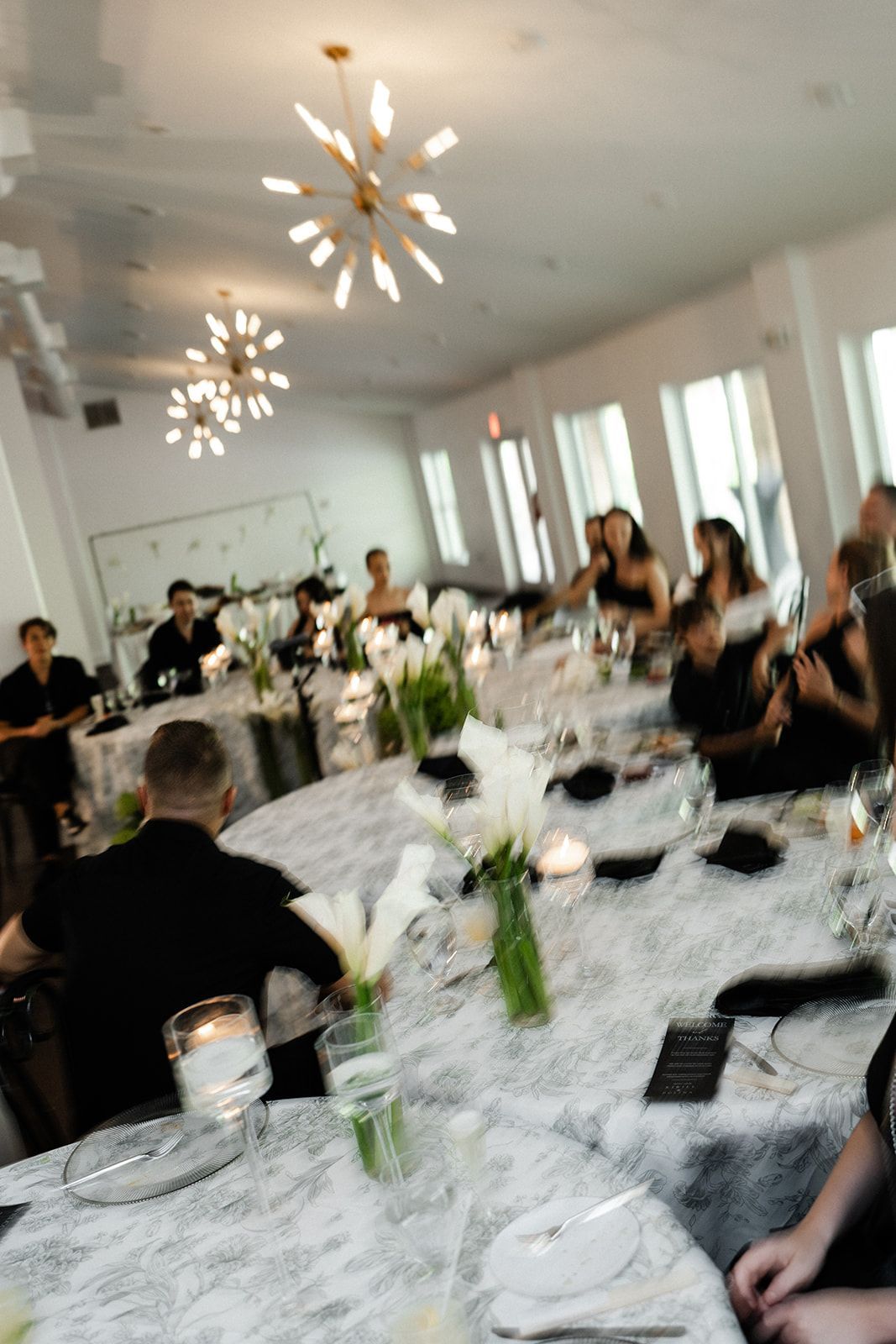 Guests seated at round tables in a brightly lit room, set for a formal dinner.