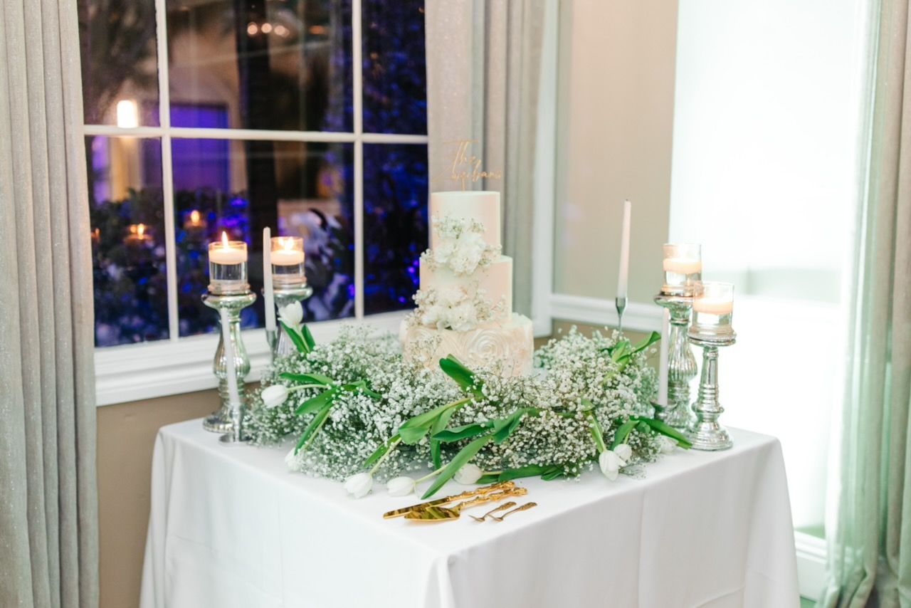 Wedding cake with floral arrangement on table with candles, near a window.